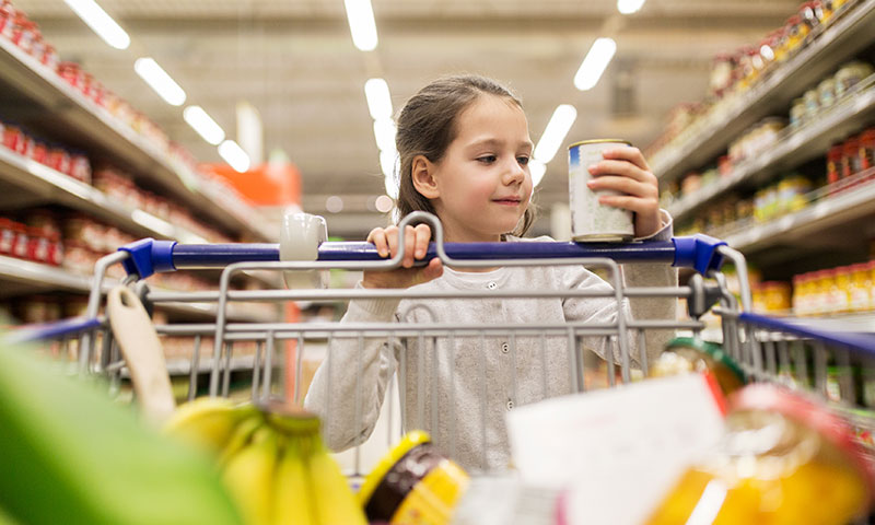 Little girl at grocery cart reading the label on a food can