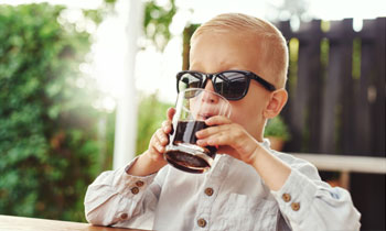 a boy in sunglasses drinking a a glass of soda