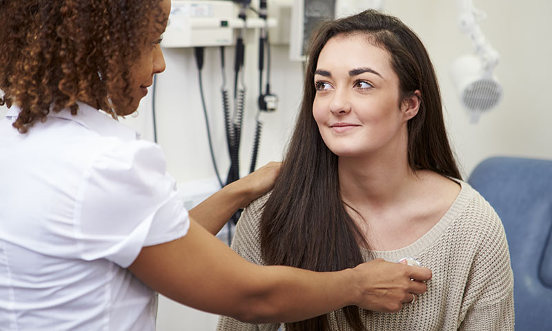 Teenage girl at the doctor while nurse listens to her heart