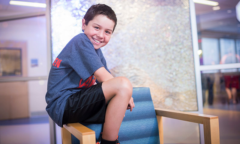 Patient Evan sitting on the arm of a chair smiling