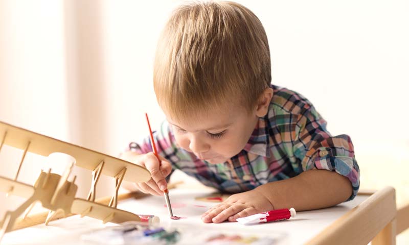 Little boy painting his wooden airplane by himself