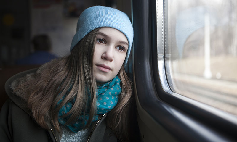 teenage girl sitting on train looking out the window