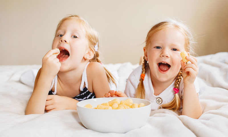 Little girls eating snack on bed