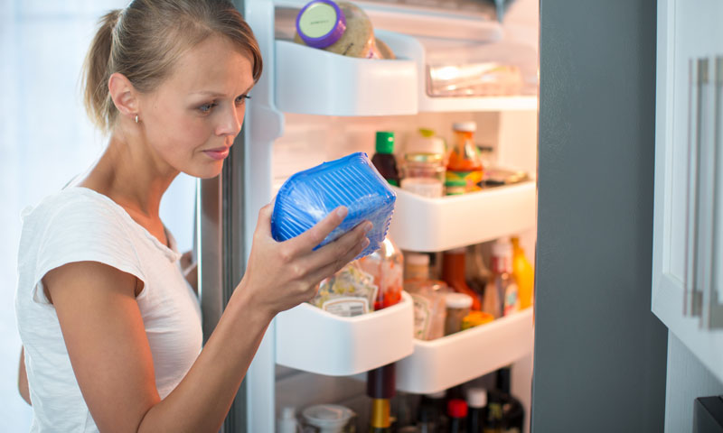 Mother checking package of food from refrigerator for expiration date