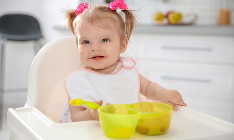 Baby eating in her high chair out of a plastic storage container