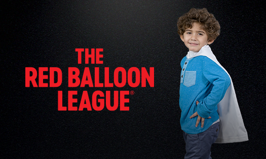 Little boy wearing a cape while supporting red balloon league