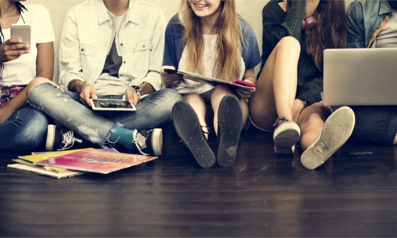a group of teens sitting on the floor using their electronic devices