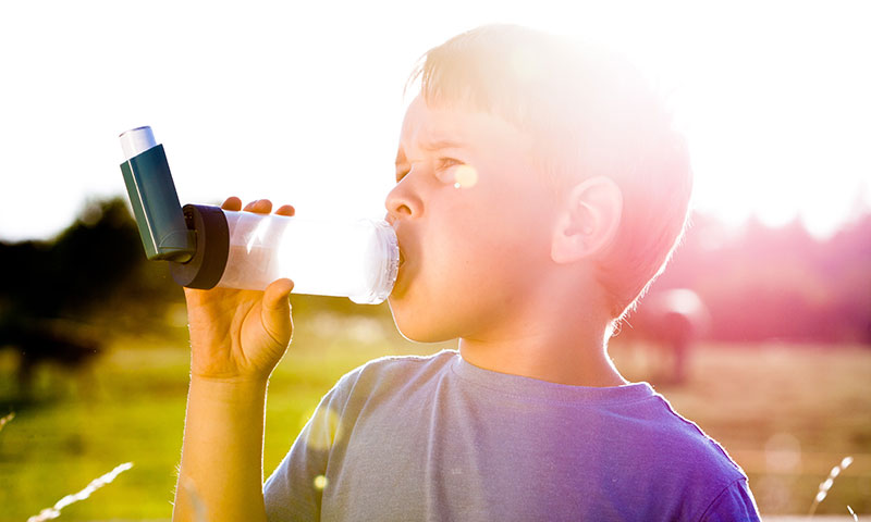 Boy using inhaler for asthma in field