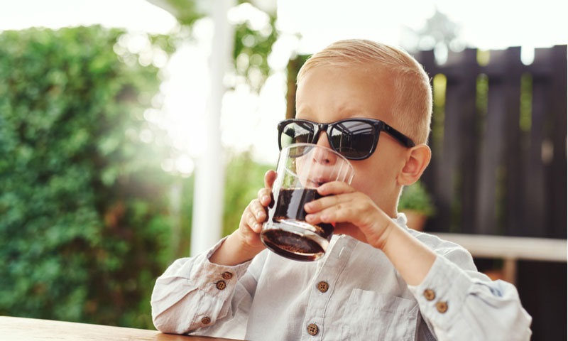 Young boy sitting on an outdoor patio sipping a soft drink