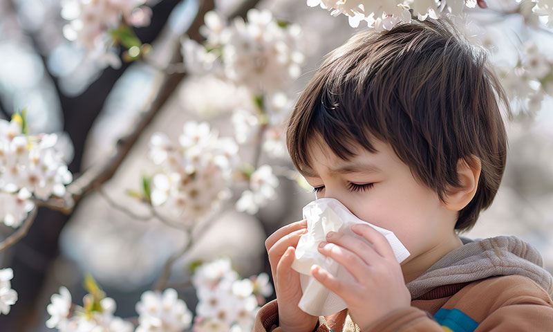 Child blowing his nose around flowers.