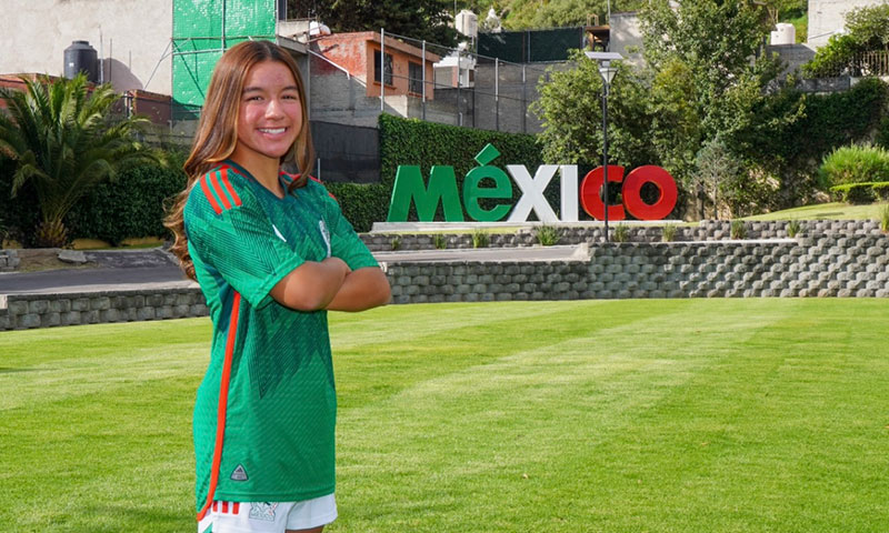 Jade standing in front of a Mexico sign while wearing a soccer jersey.