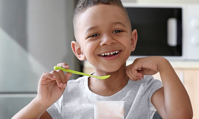 Little boy eating yogurt at kitchen table