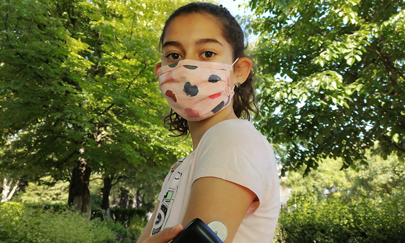 young girl wearing a mask while checking glucose levels
