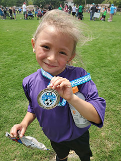 Little girl holding her medal while smiling