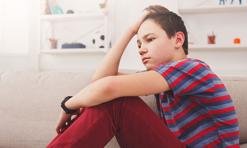 Teenage boy sitting holding his head