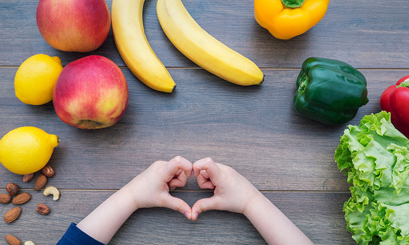 Hands are made into a heart while showing fruits and vegetables