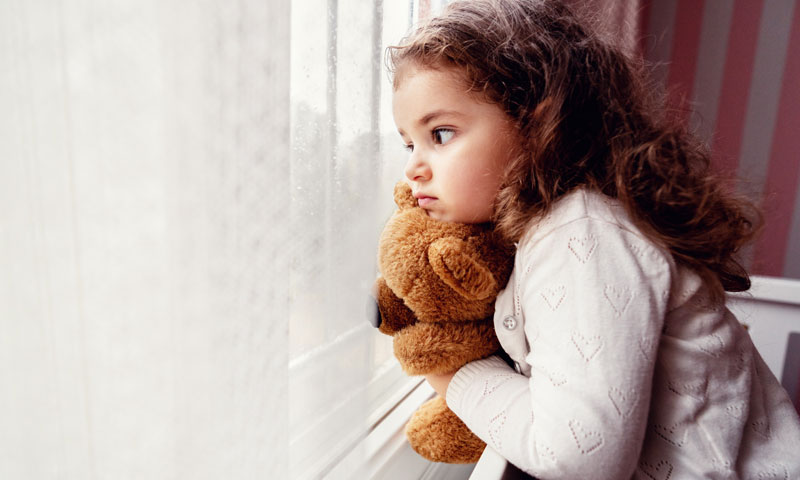 Little girl watching rain with teddy bear