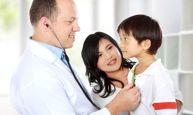 Doctor listening to little boys heart while his mom stands next to them.