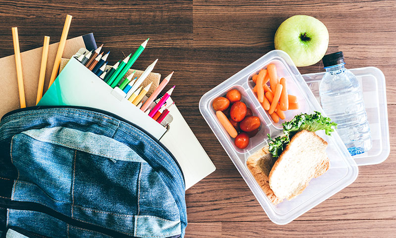 back pack with school supplies next to a nutritional lunch