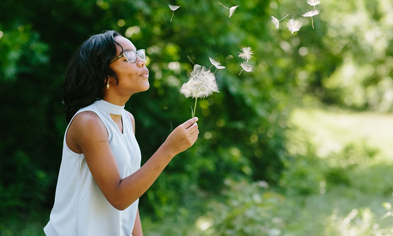 Jasmin making a wish on a dandelion and blowing the seeds into the wind 
