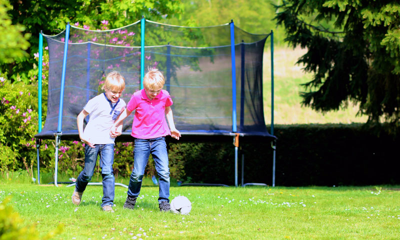 Laughing children playing in the backyard with a trampoline in the background