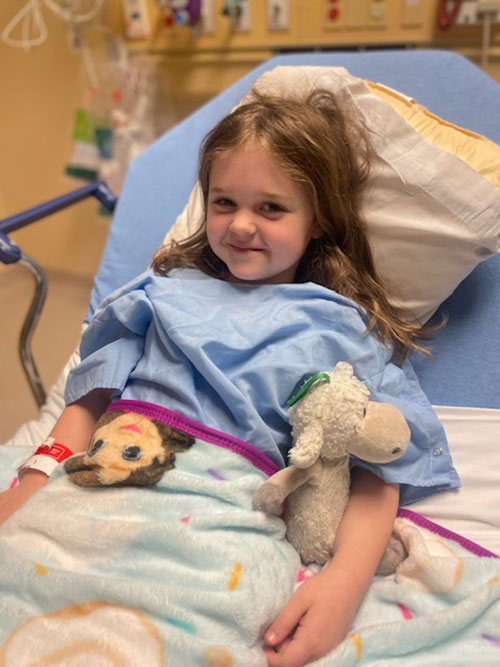 Little girl in hospital bed holding a stuffed animal.