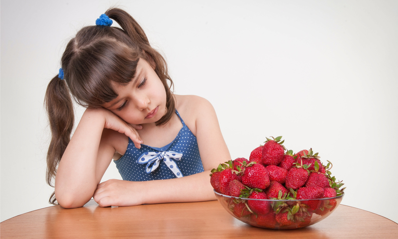 Little girl sitting at a table looking at bowl of strawberries