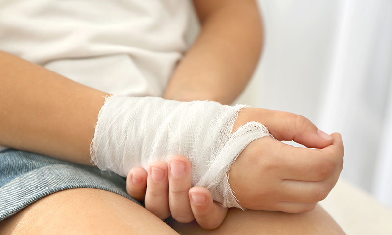 Little girl holding injured hand wrapped in bandage