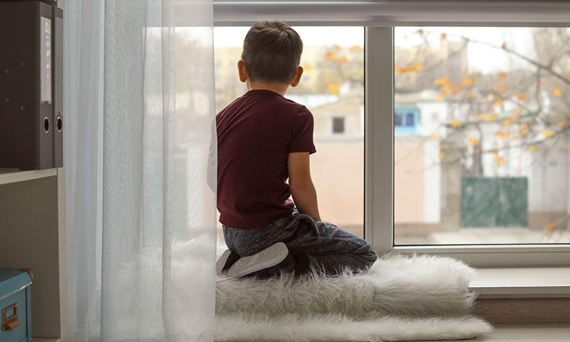 young boy sitting by the window looking outside