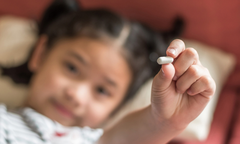 Child in bed holding up a pill
