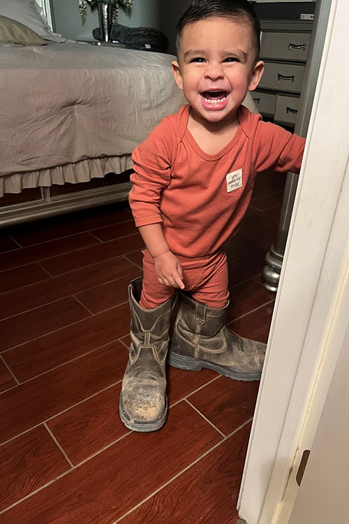 Little boy smiling while wearing large work boots.