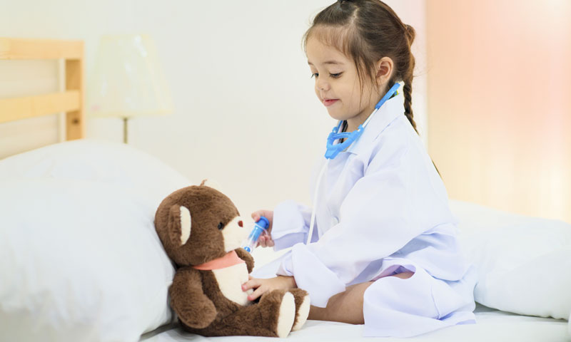 Little girl playing doctor giving her teddy bear a vaccine shot