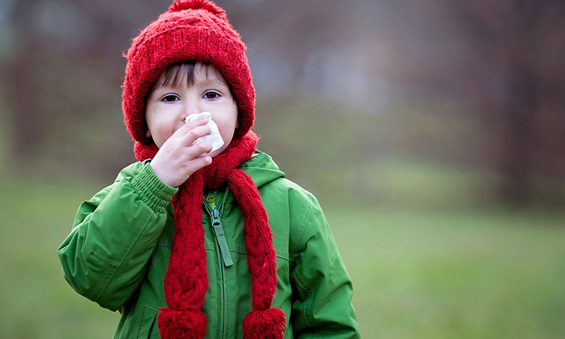 Boy outdoors blowing nose on winter day