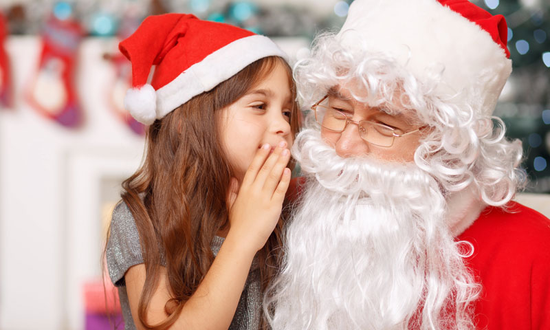 Little girl on Santa's lap whispering what she wants in his ear