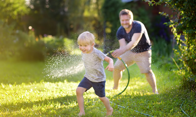 Little boy playing in yard with water hose with father