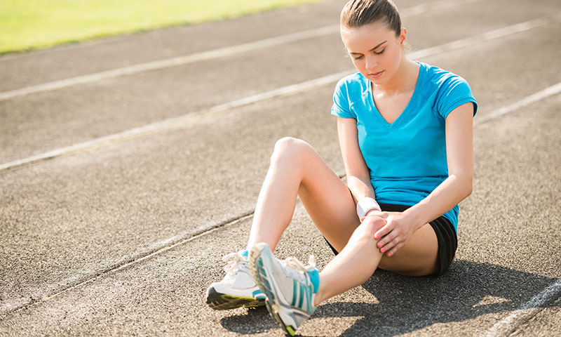 Teen girl sitting on a running track holding her knee