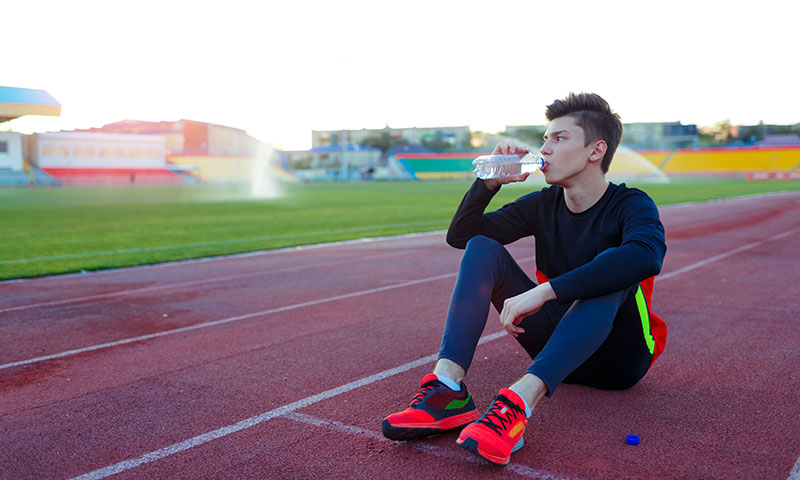 Teen athlete drinking water at running track