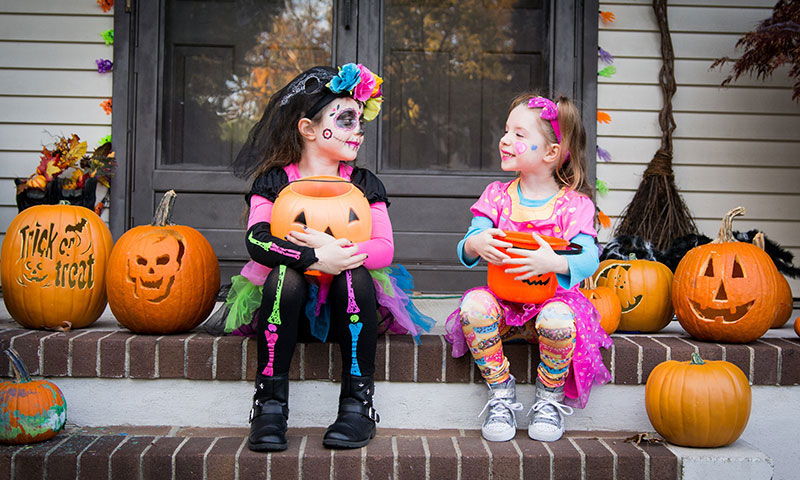 Children in Halloween costumes on front steps with pumpkins