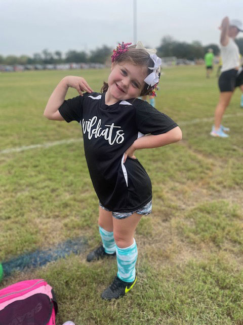 Little girl on a soccer field flexing her muscles.