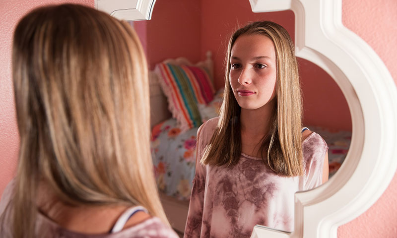 Teenage girl looking at herself in the mirror
