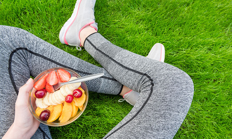 Young athlete sitting in the grass eating a bowl of colorful fruit