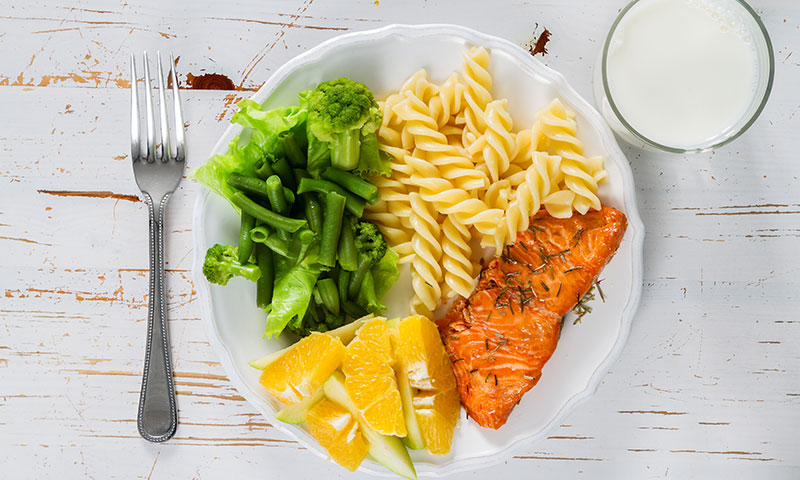 Healthy portioned plate with salmon,pasta, greens, fruits and milk
